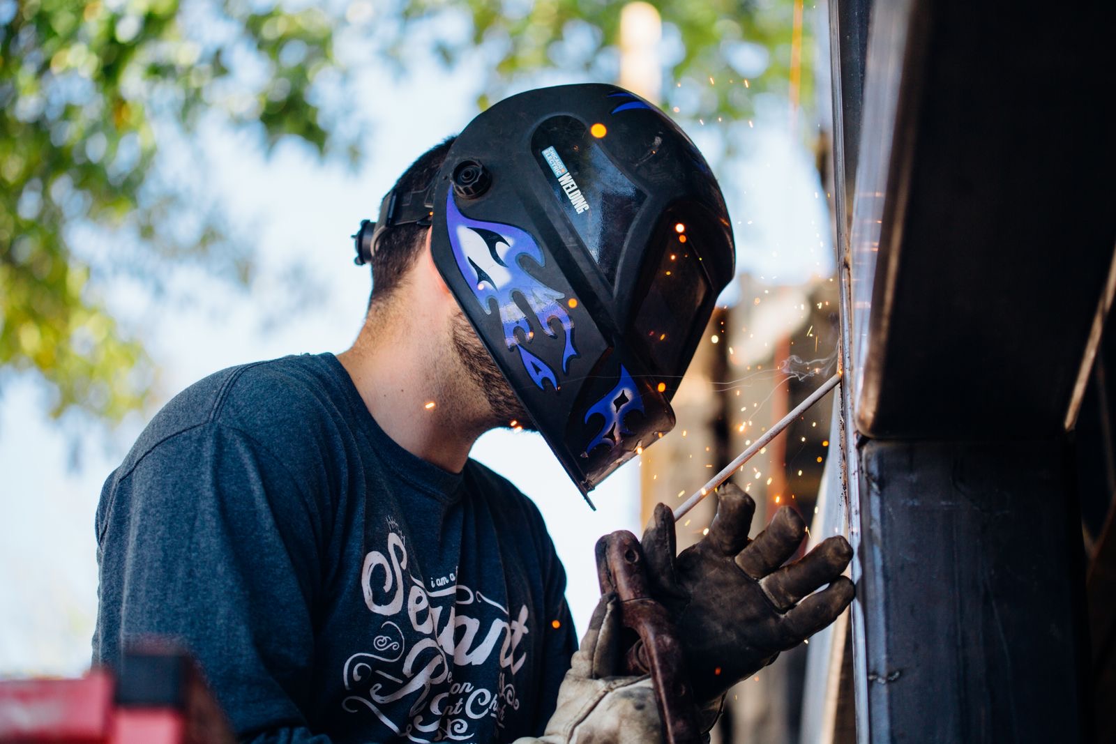 Apprentice welder in a helmet working outdoors with sparks flying